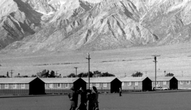 a black and white photo of people walking to barracks in manzanar